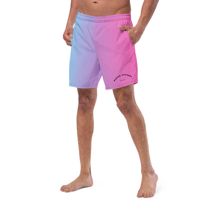 Man wearing swim trunks with a light-blue-to-pink design and a black 'Breeze Apparel Miami' word logo on the bottom-left knee