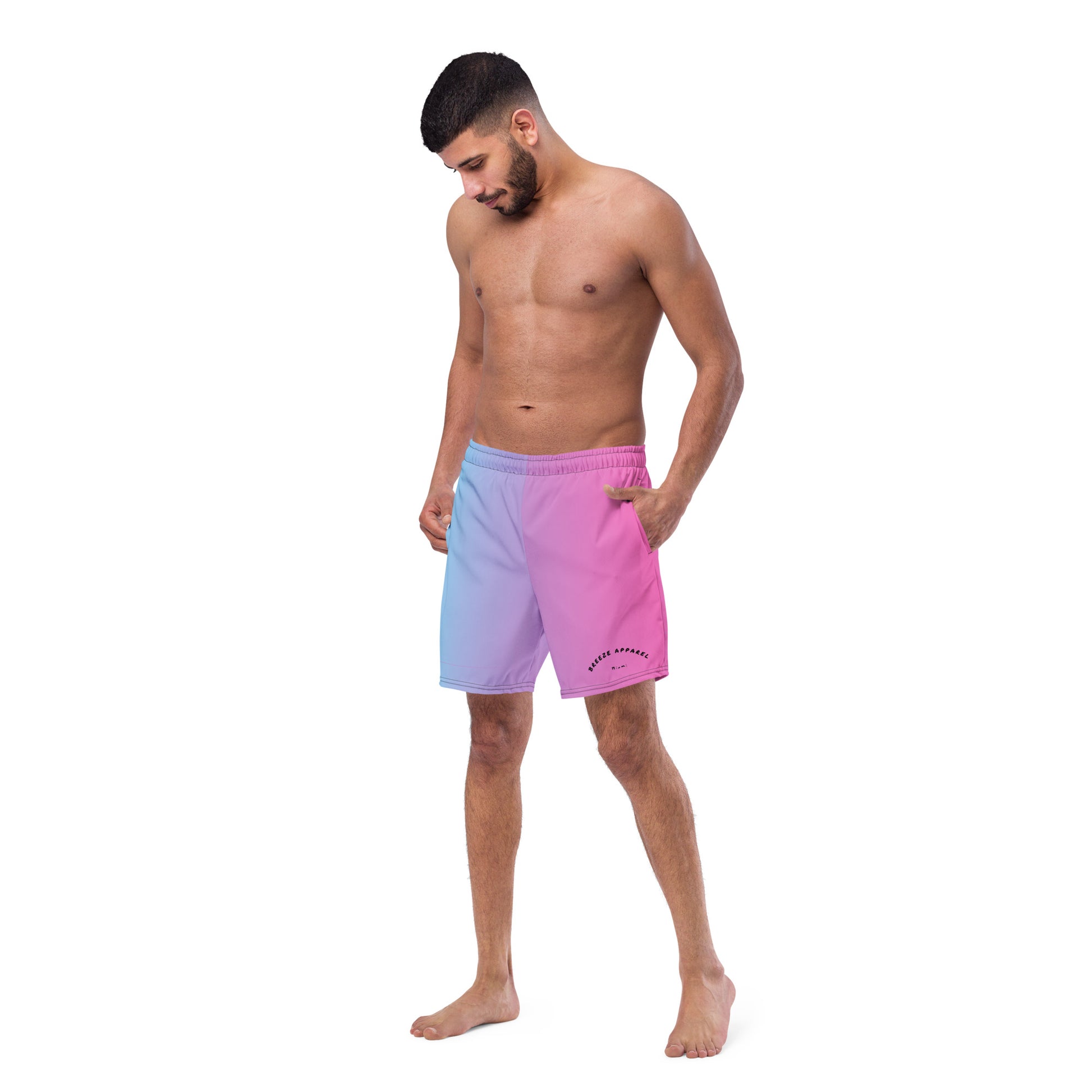 Man wearing swim trunks with a light-blue-to-pink design and a black 'Breeze Apparel Miami' word logo on the bottom-left knee