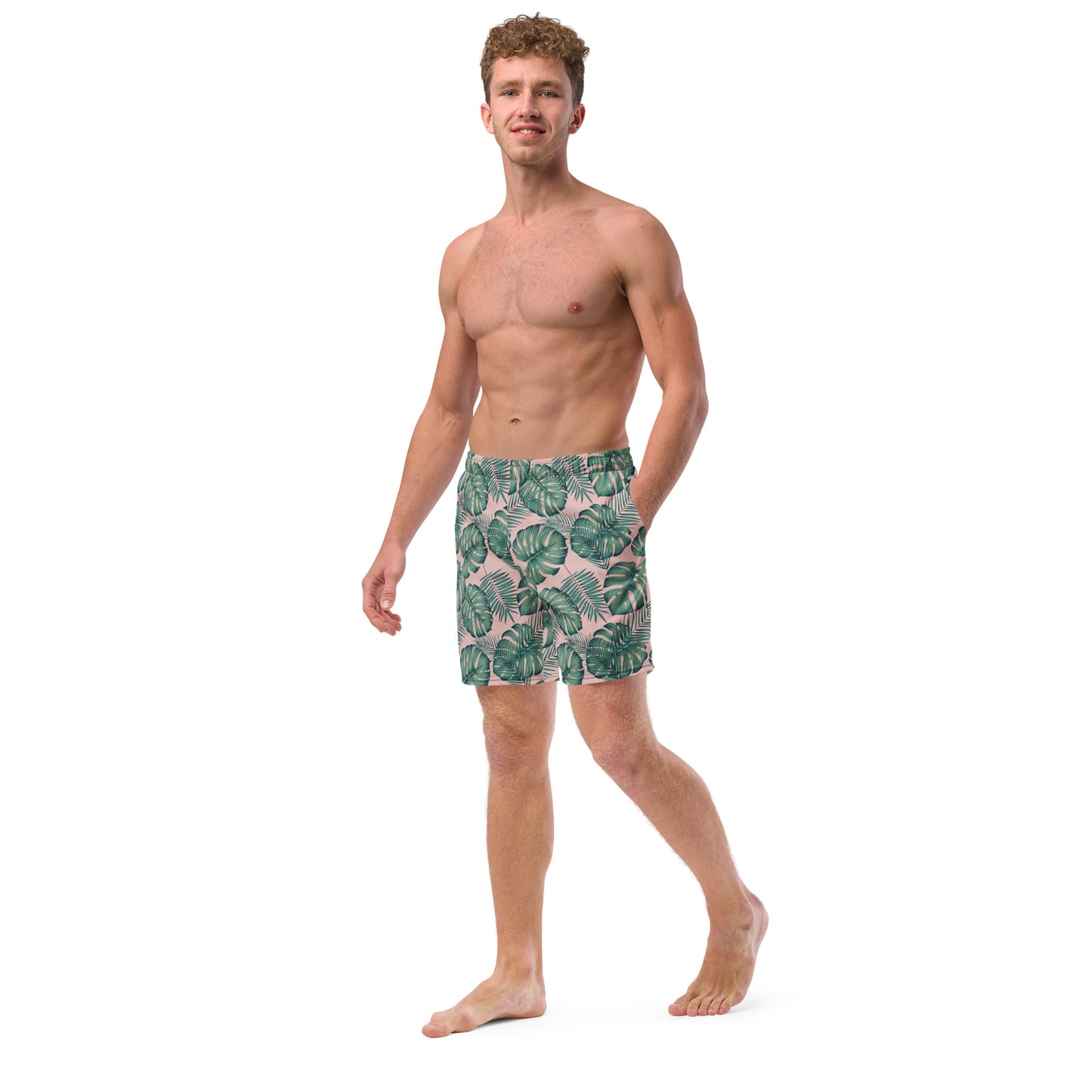 Man wearing swim trunks with pattern of green palm leaves set on a pink background.