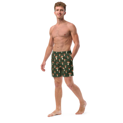 Man wearing swim trunks with pattern of mushrooms on a green background.
