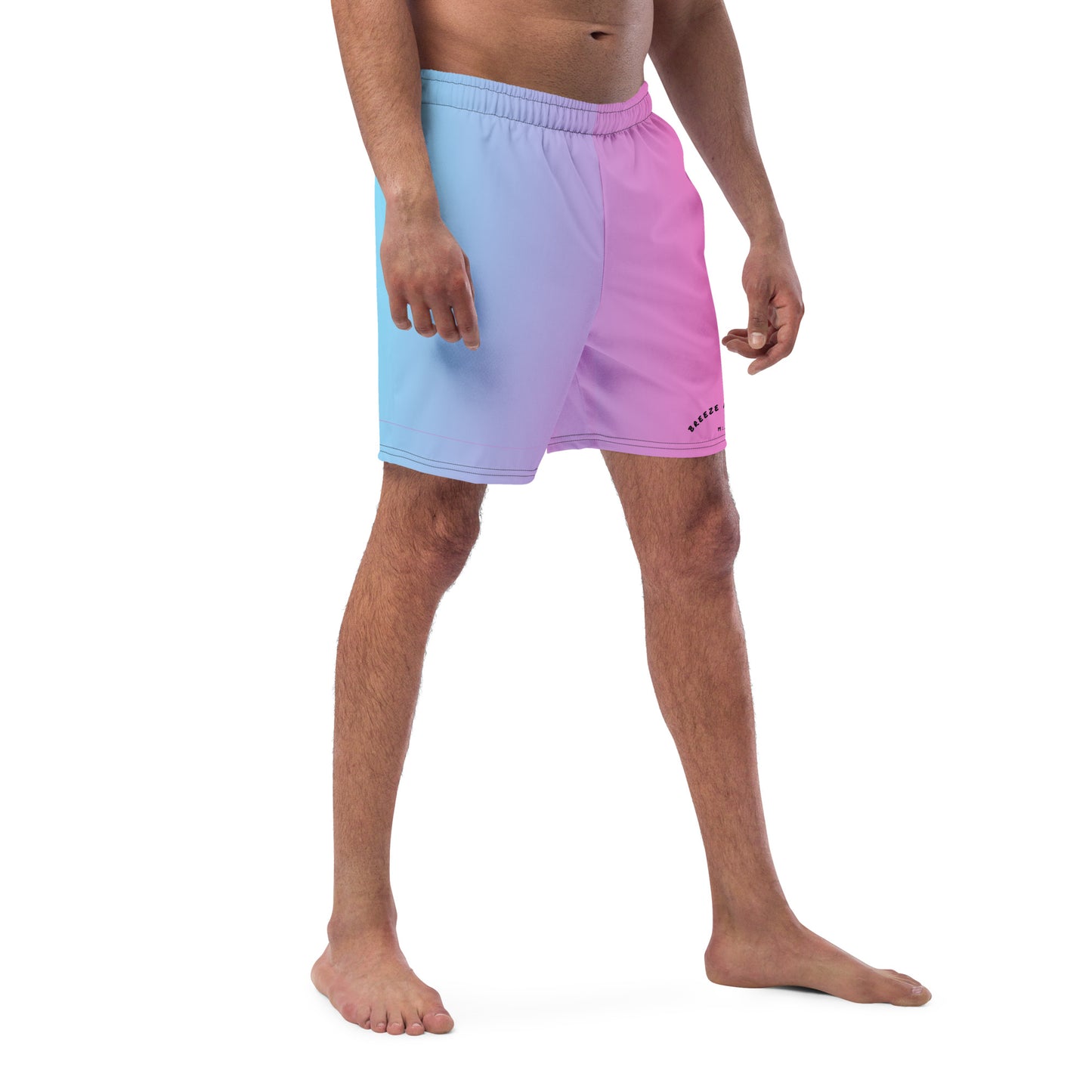 Man wearing swim trunks with a light-blue-to-pink design and a black 'Breeze Apparel Miami' word logo on the bottom-left knee