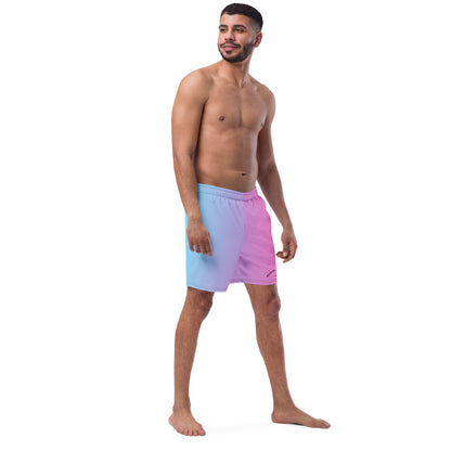 Man wearing swim trunks with a light-blue-to-pink design and a black 'Breeze Apparel Miami' word logo on the bottom-left knee