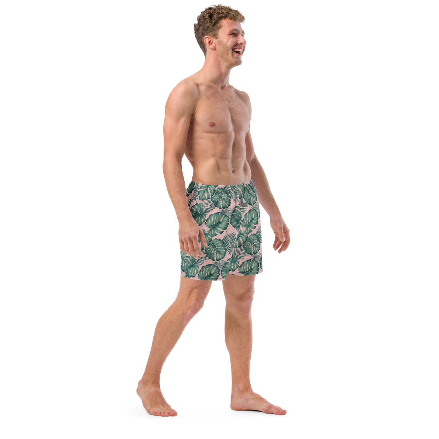 Man wearing swim trunks with pattern of green palm leaves set on a pink background.