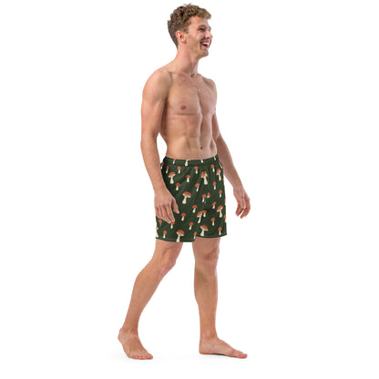Man wearing swim trunks with pattern of mushrooms on a green background.