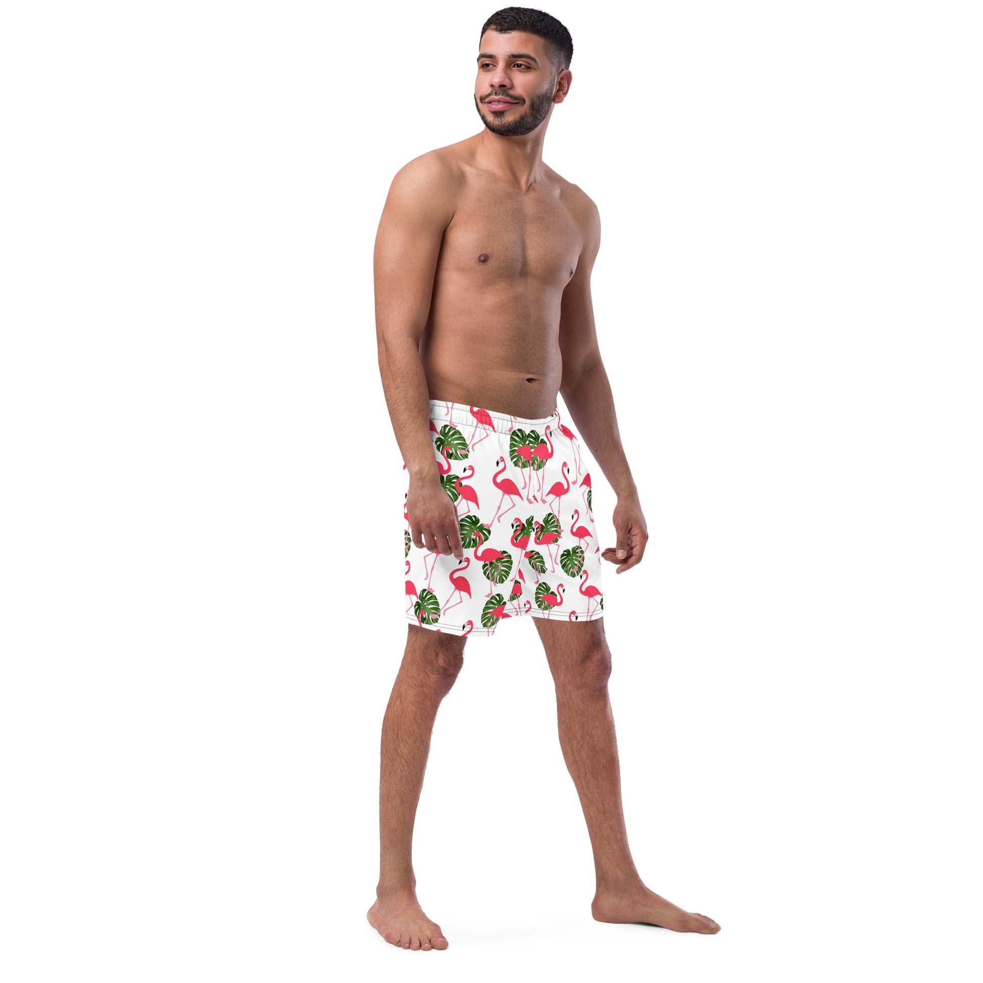 Man wearing swim trunks with pattern of pink flamingos and green leaves set on a white background.