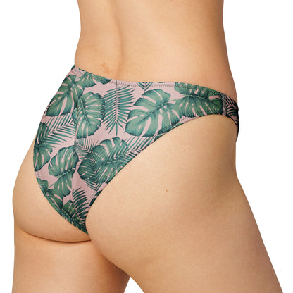 Rear view of woman wearing bikini bottom with design of green palm leaves set on a pink background.
