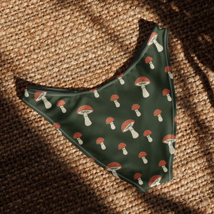 Back of bikini bottom with all-over design of mushrooms set on a dark-green background, laying in the sunlight.