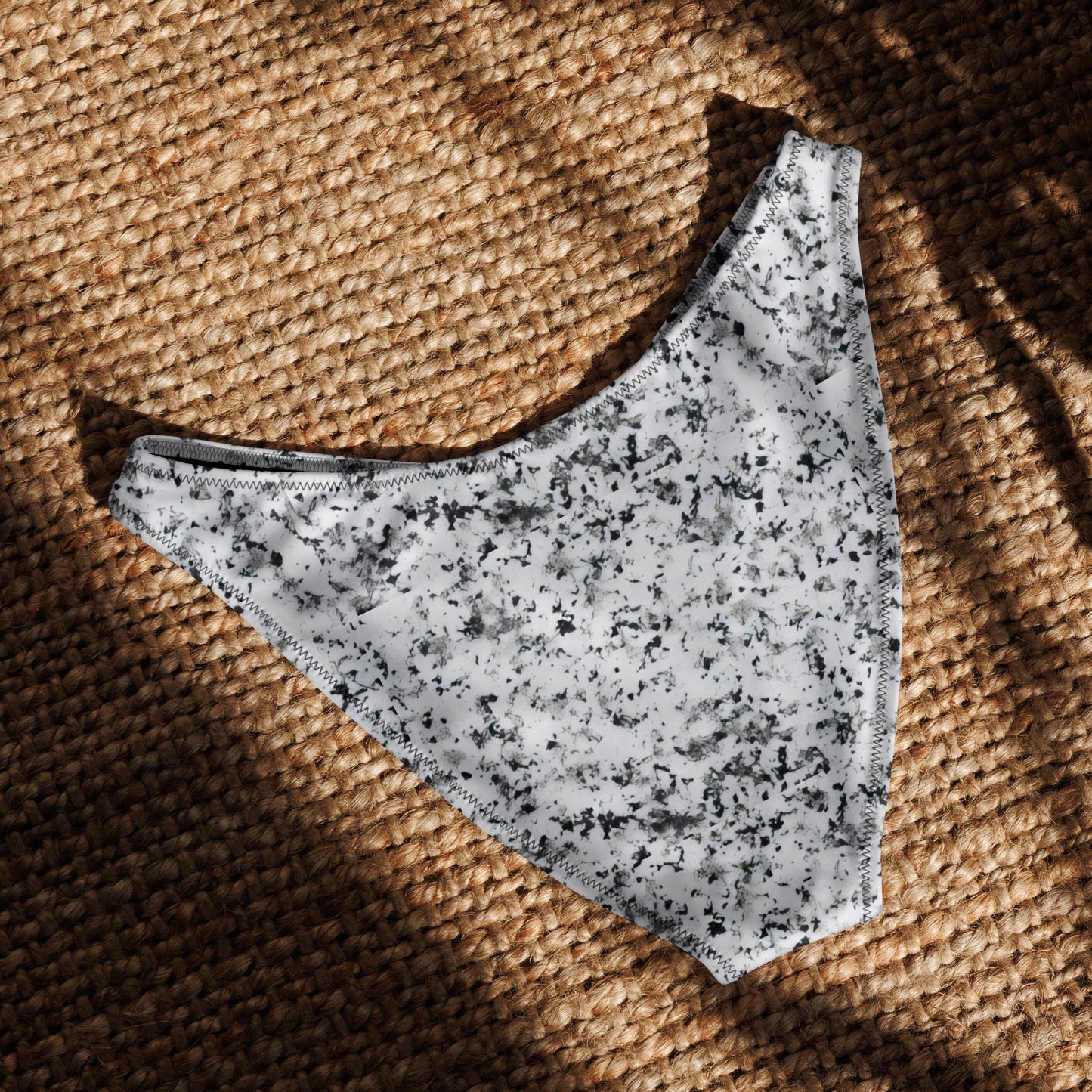 Back of bikini bottom with pattern of black splotches set on white background, laying in sunlight.