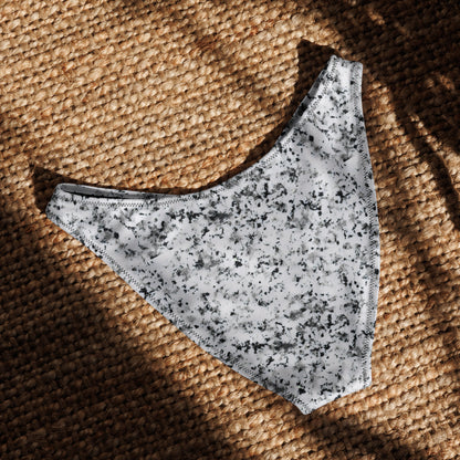 Back of bikini bottom with pattern of black splotches set on white background, laying in sunlight.