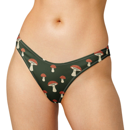 Woman wearing bikini bottom with all-over design of mushrooms set on a dark-green background, laying in the sunlight.