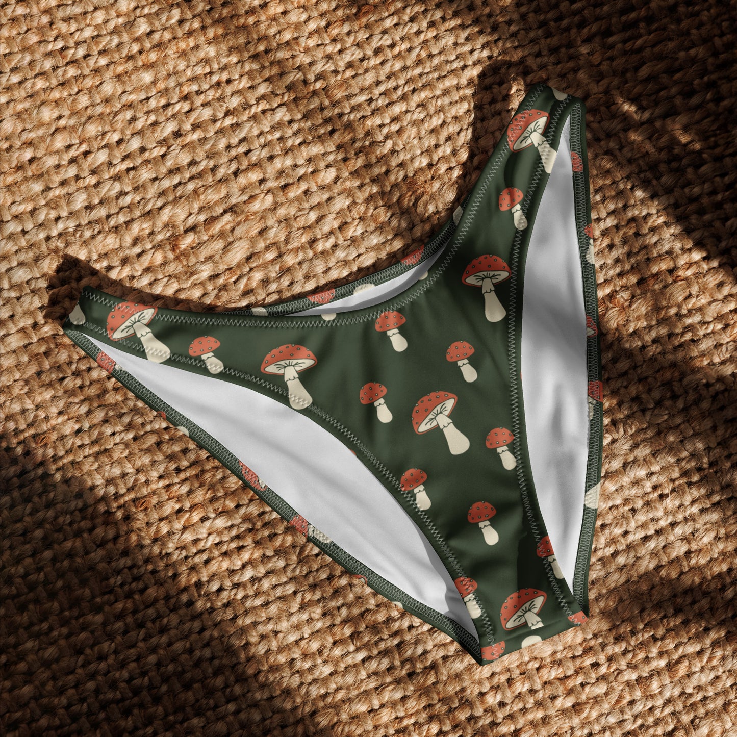 Bikini bottom with all-over design of mushrooms set on a dark-green background, laying in the sunlight.