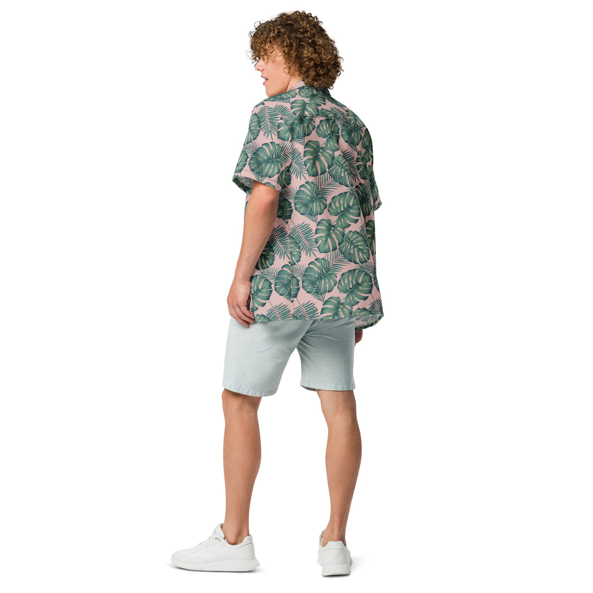 Rear view of man wearing button-down shirt with pattern of green palm leaves set on a pink background.
