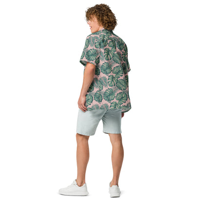 Rear view of man wearing button-down shirt with pattern of green palm leaves set on a pink background.