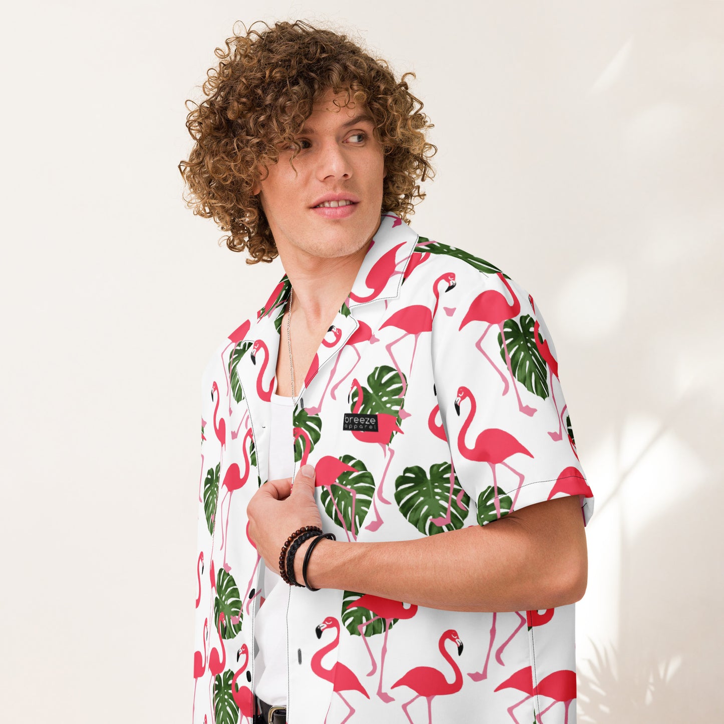 Man wearing button-down shirt with pattern of flamingos and green palm leaves set on a white background.