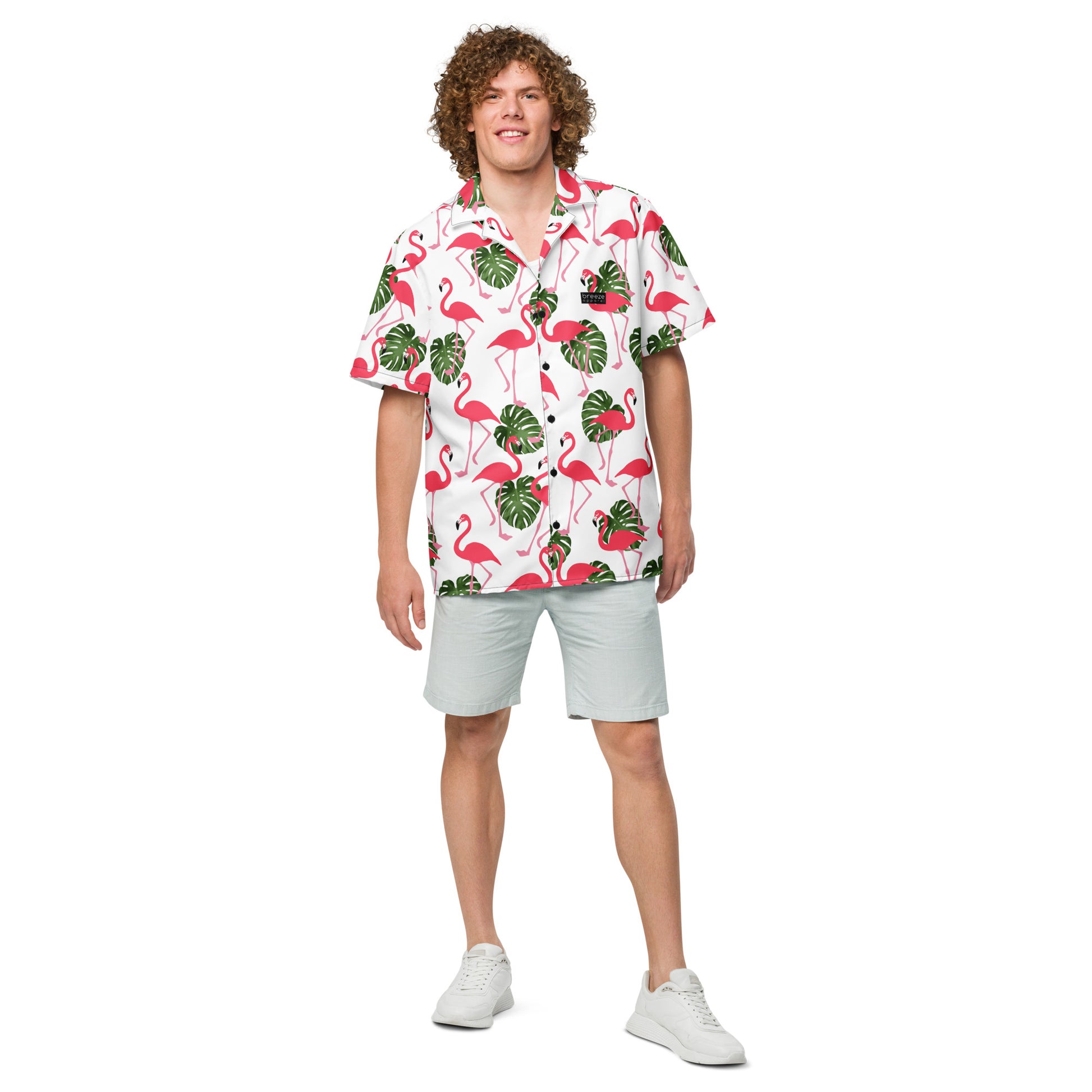 Man wearing button-down shirt with pattern of flamingos and green palm leaves set on a white background.