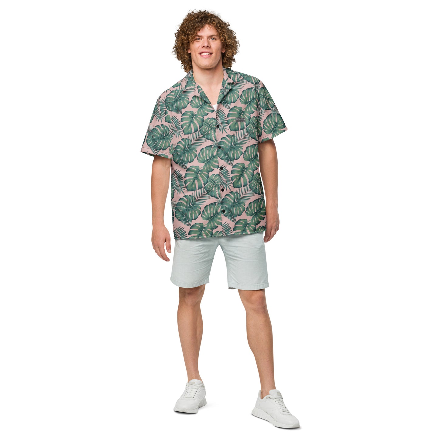 Man wearing button-down shirt with pattern of green palm leaves set on a pink background.