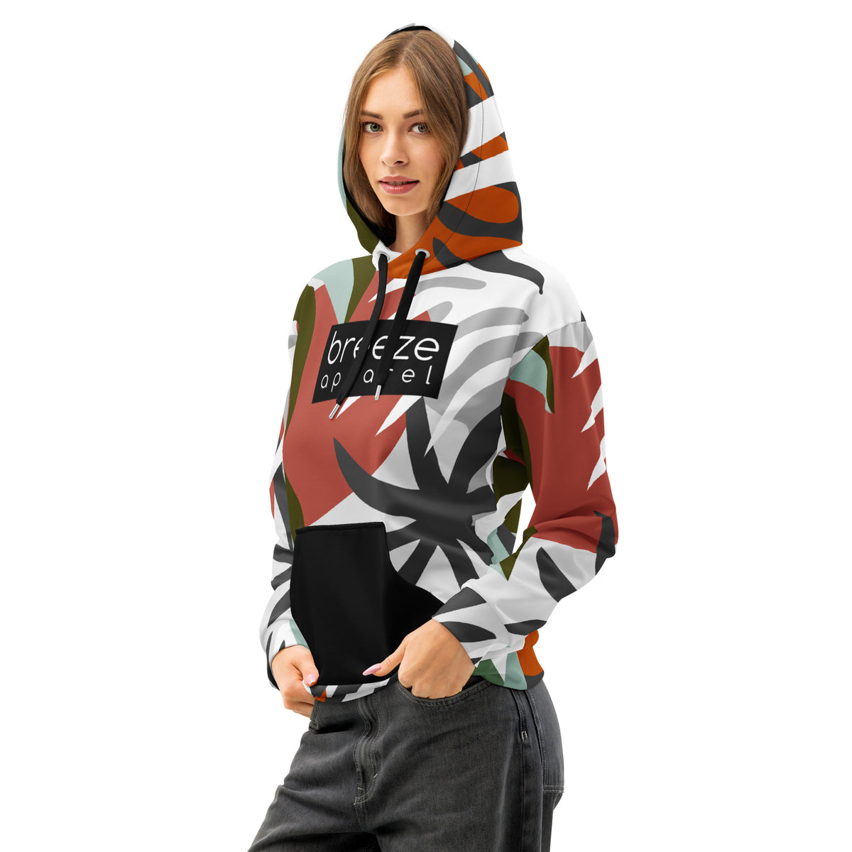 Woman wearing hoodie with a red, black, green, orange, and white floral-geometric design, with a black pocket, black drawstrings, and a 'breeze apparel' logo  consisting of white wording set in a black rectangle across the chest.