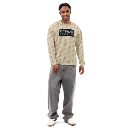 Man wearing beige sweatshirt with pattern of green geckos. Across chest is black, rectangular logo with white lettering.