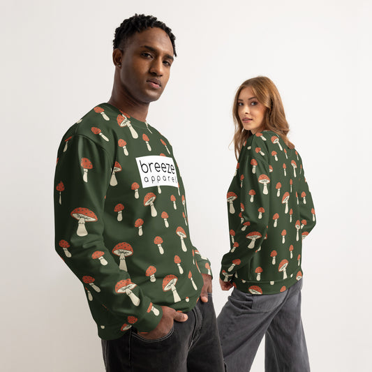 Man and woman, each wearing a forest-green sweatshirt with an all-over mushroom pattern. A white rectangle with 'breeze apparel' written in black inside is across the chest. Front is shown on man; backside is shown on woman.