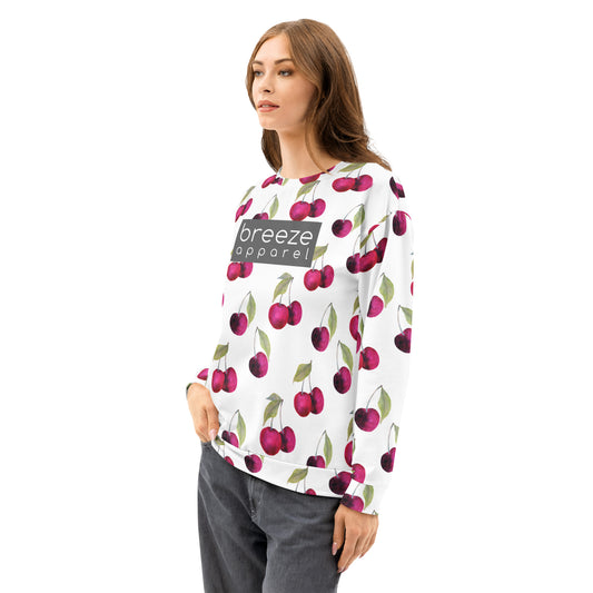 Woman wearing a white sweatshirt with an all-over cherries design. Across the chest is a gray rectangle with 'breeze apparel' in white inside.