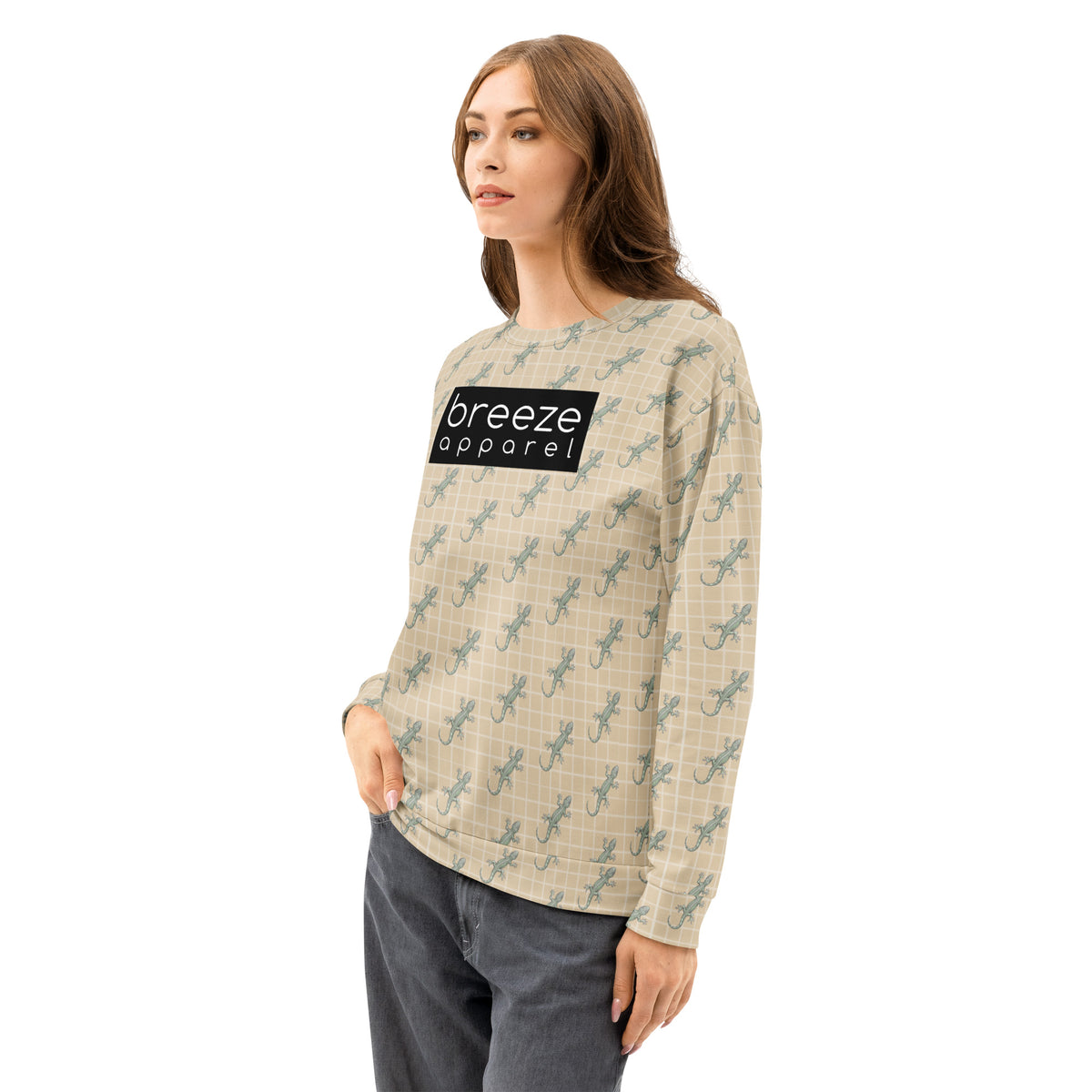 Woman wearing beige sweatshirt with pattern of green geckos. Across chest is black, rectangular logo with white lettering.