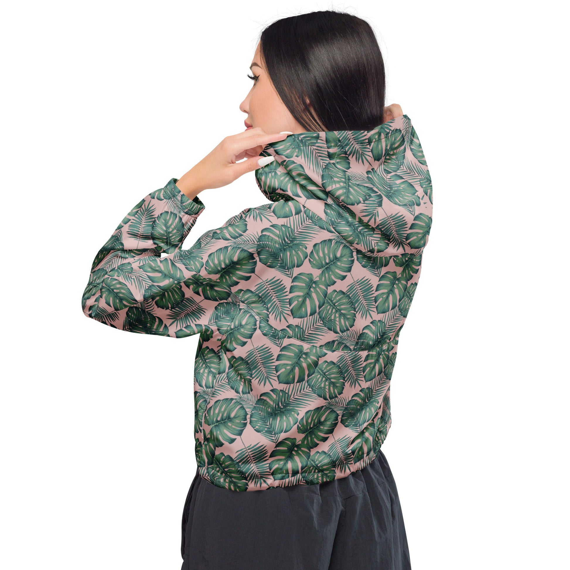 Rear view of woman wearing cropped jacket with pattern of green palm leaves set on a pink background.