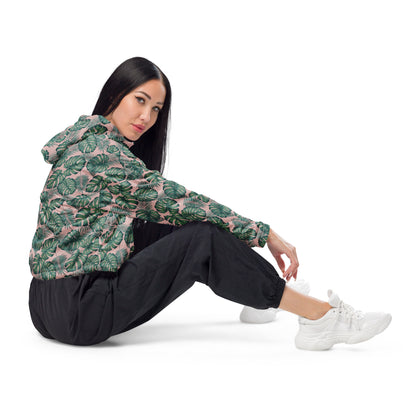 Woman wearing cropped jacket with pattern of green palm leaves set on a pink background.