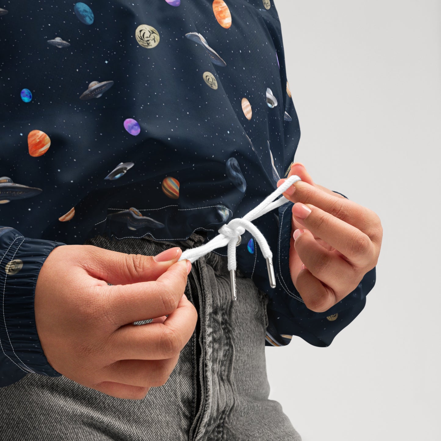 Woman wearing cropped windbreaker with pattern of UFOs and planets in space.