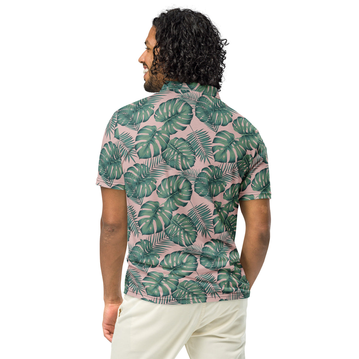 Rear view of man wearing polo with pattern of green palm leaves set on a light-pink background.