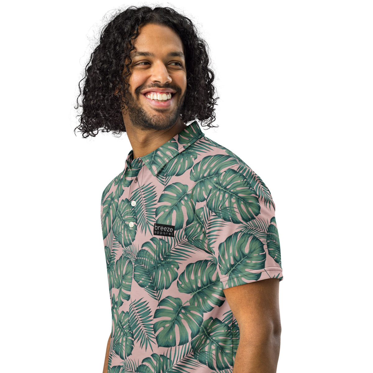Man wearing polo with pattern of green palm leaves set on a light-pink background.