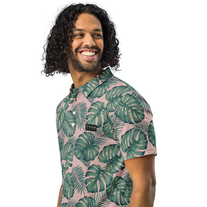 Man wearing polo with pattern of green palm leaves set on a light-pink background.