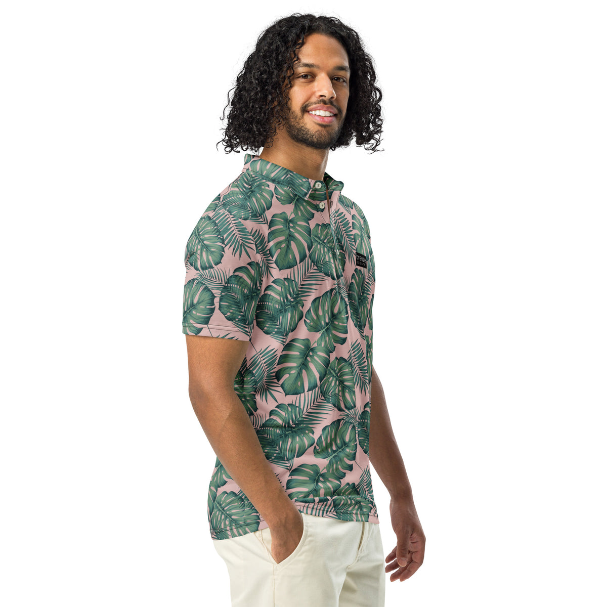 Man wearing polo with pattern of green palm leaves set on a light-pink background.