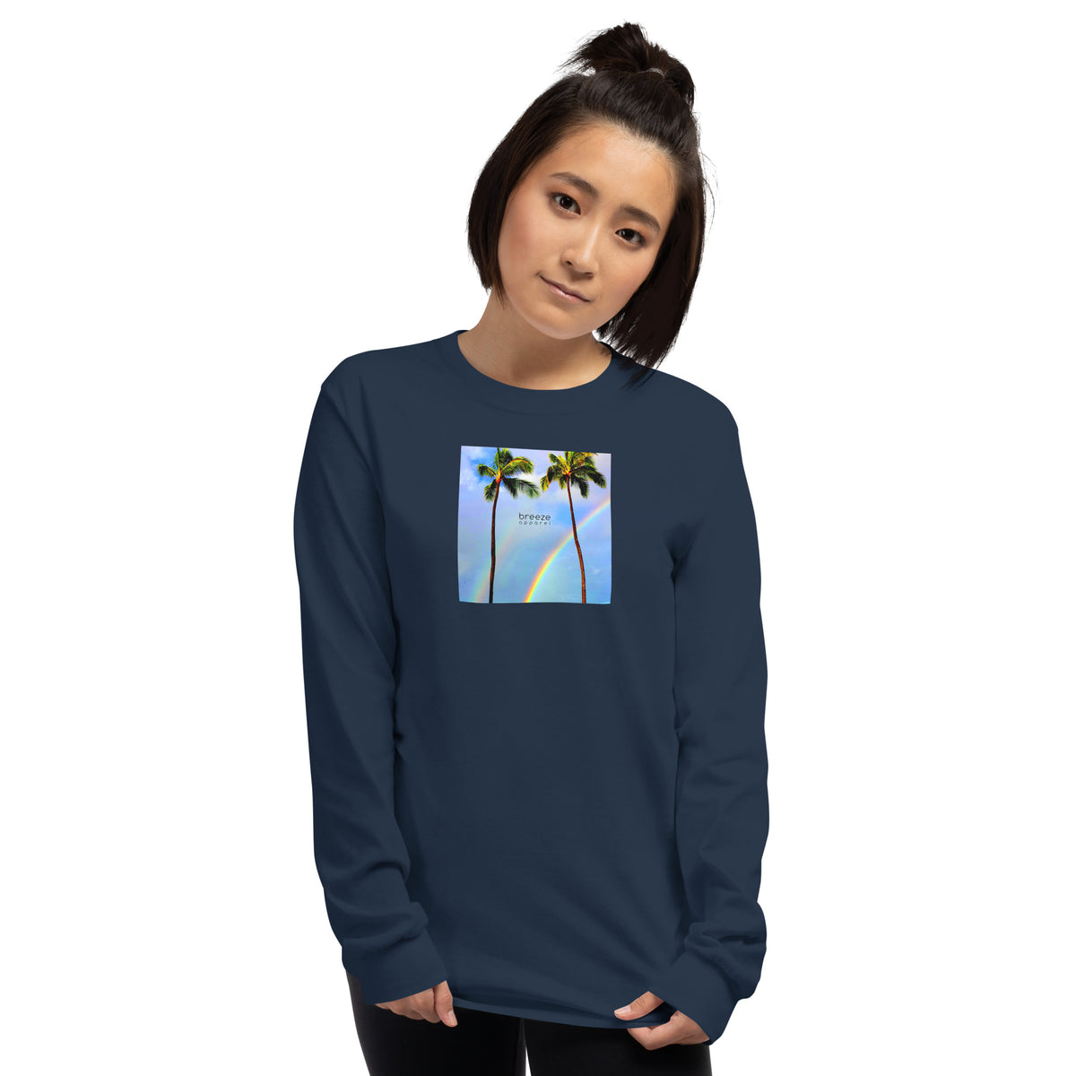 Woman wearing navy long-sleeved shirt with a graphic of palm trees, rainbow, and a clear blue sky in the background. A small, black 'breeze apparel' logo is between the trees.