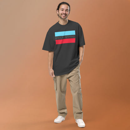 Man wearing gray, oversized t-shirt with graphic of gray lettering between light-blue and red stripes.