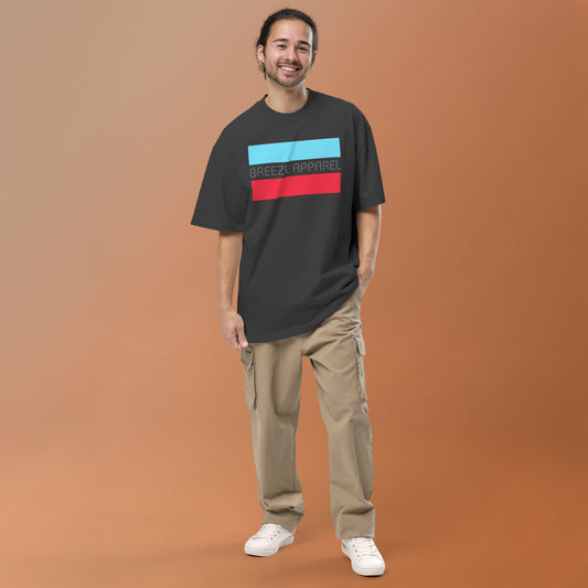 Man wearing gray, oversized t-shirt with graphic of gray lettering between light-blue and red stripes.