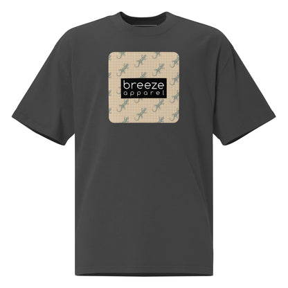 Gray t-shirt with square over chest that contains pattern of green geckos set on beige background, overlaid with black, rectangular logo with white lettering.