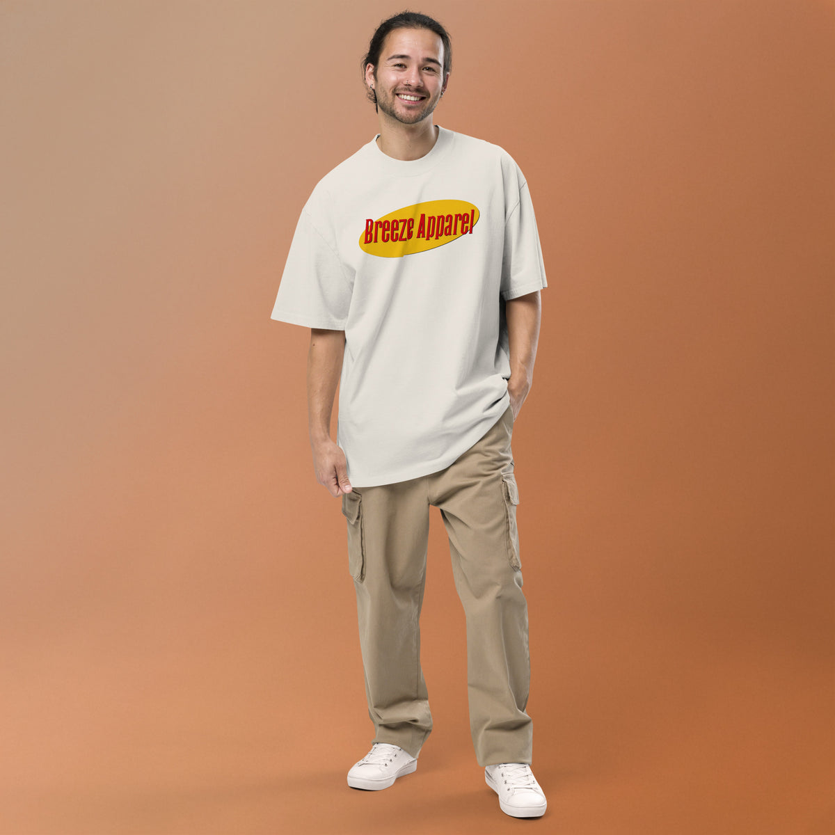 Man wearing white, oversized t-shirt with graphic of red lettering set over yellow oval.