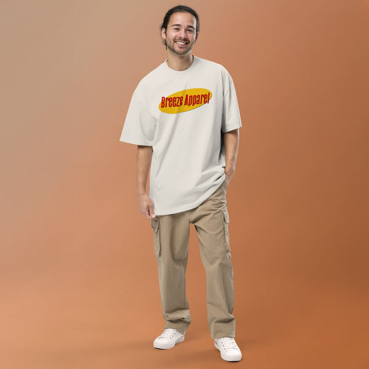 Man wearing white, oversized t-shirt with graphic of red lettering set over yellow oval.