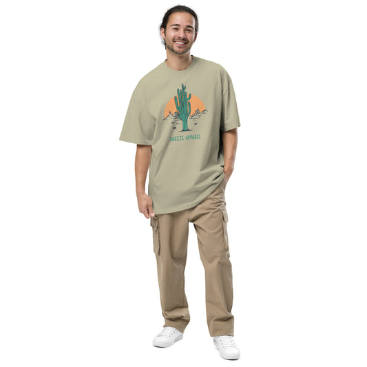 Man wearing green, oversized t-shirt with graphic of cactus and sunset.