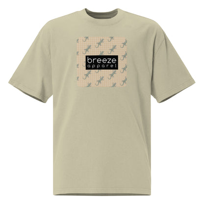Green t-shirt with square over chest that contains pattern of green geckos set on beige background, overlaid with black, rectangular logo with white lettering.