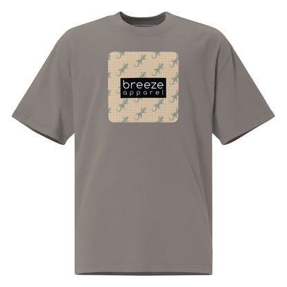Gray t-shirt with square over chest that contains pattern of green geckos set on beige background, overlaid with black, rectangular logo with white lettering.