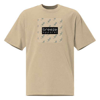 Brown t-shirt with square over chest that contains pattern of green geckos set on beige background, overlaid with black, rectangular logo with white lettering.