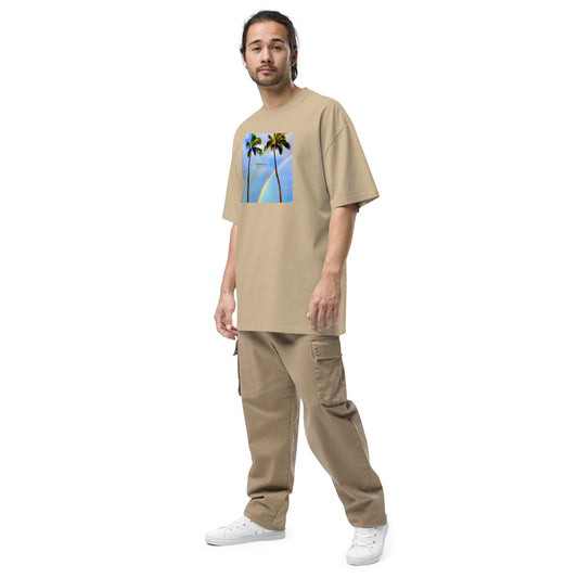 Man wearing tan, oversized t-shirt with graphic of two palm trees and rainbow in background.