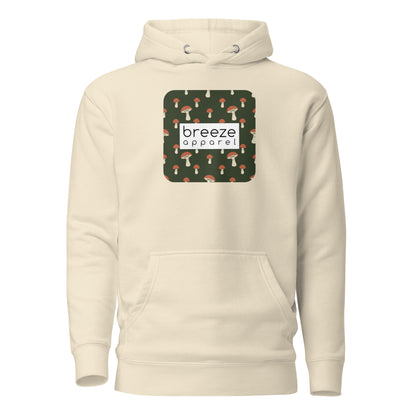 Beige hoodie with graphic of mushrooms set on a green background and overlaid with a white, rectangular logo.