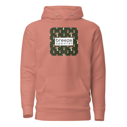 Pink hoodie with graphic of mushrooms set on a green background and overlaid with a white, rectangular logo.