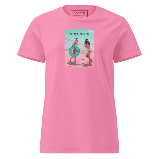 Pink t-shirt with an image of two women in bikinis on the beach, standing by a volleyball net, one holding a swim ring and smiling, the other leaning on the net, with inscription in black of 'breeze apparel' towards the top of the image, and 'fun in the sun' in black on the ground between the women. 