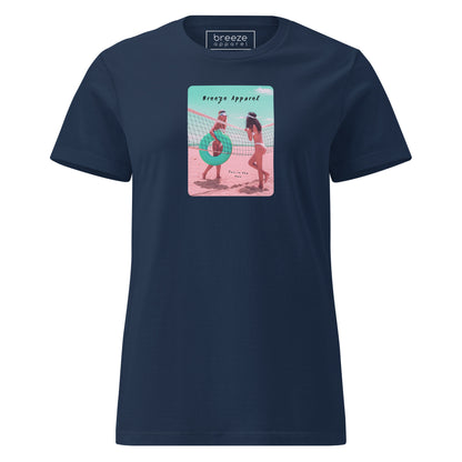 Navy t-shirt with an image of two women in bikinis on the beach, standing by a volleyball net, one holding a swim ring and smiling, the other leaning on the net, with inscription in black of 'breeze apparel' towards the top of the image, and 'fun in the sun' in black on the ground between the women. 