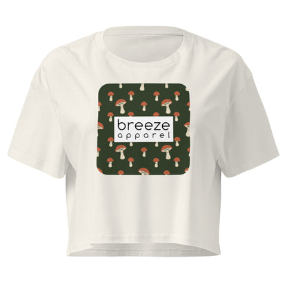 Cream crop top with graphic of mushrooms set on a green background and overlaid with a white rectangle logo.