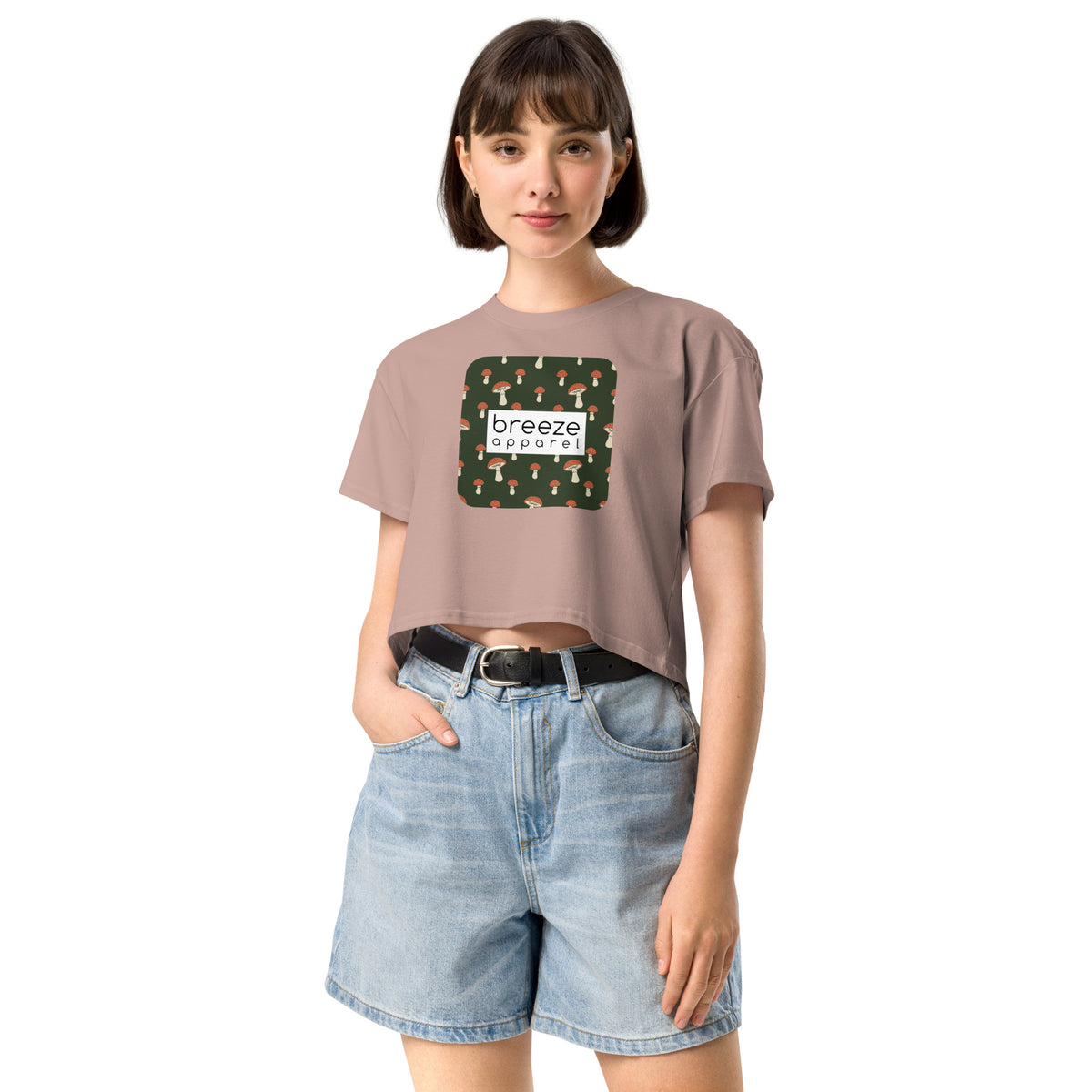 Woman wearing pink crop top with graphic of mushrooms set on a green background and overlaid with a white rectangle logo.