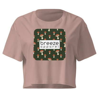 Mauve crop top with graphic of mushrooms set on a green background and overlaid with a white rectangle logo.